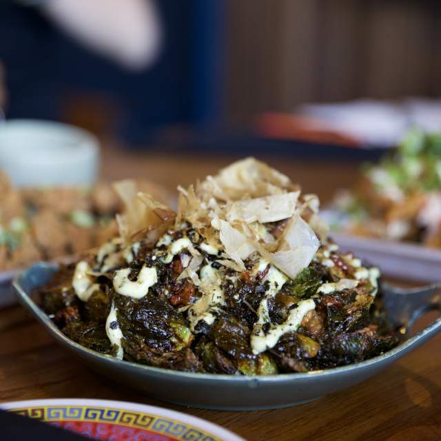 Bowl of wok-fried brussel sprouts sitting on table with other appetizers in the background.