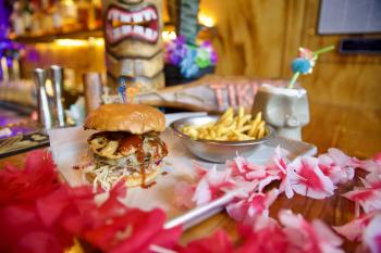 Burger, fries and drink sitting on table with tiki decorations