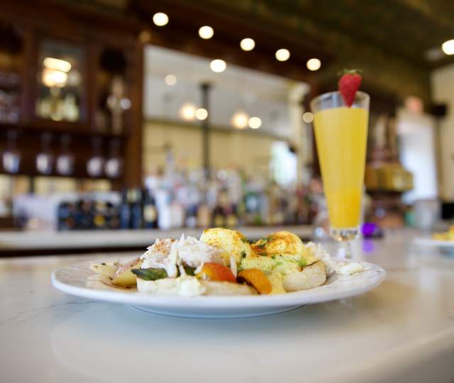 A plate of breakfast and a mimosa with a strawberry garnish sit on a restaurant bar