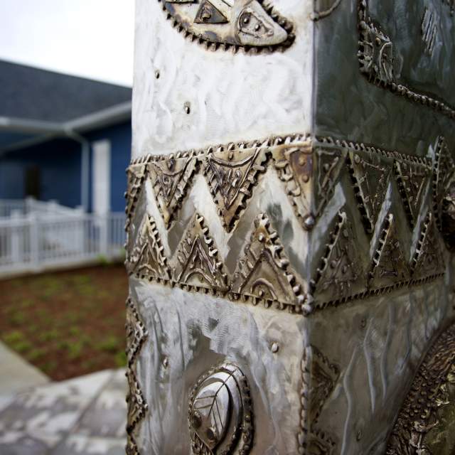 steel sculpture in front of blue building with white trim