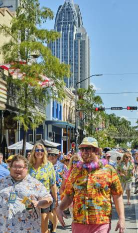 People dressed in tropical clothes walk down Dauphin Street