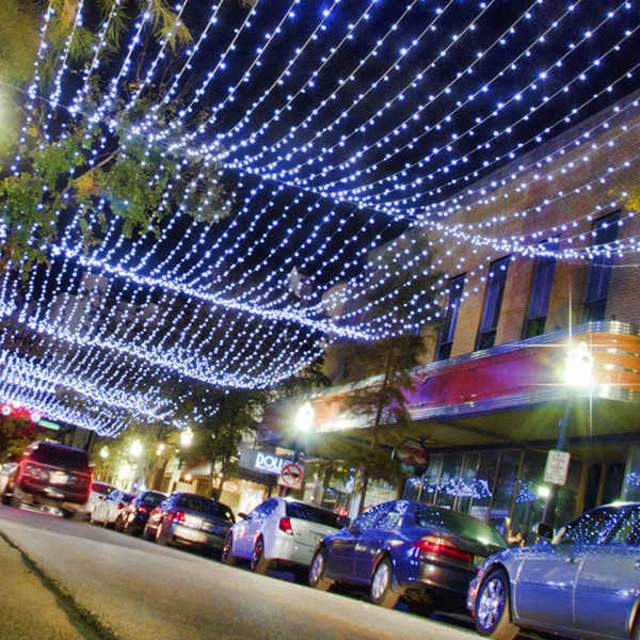 a street full of cars outside of restaurants with strings of lights overhead