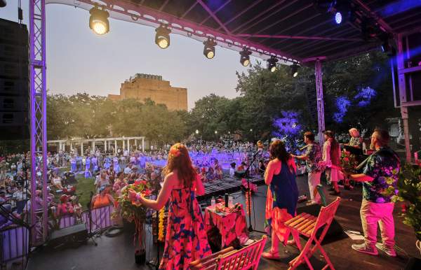 Group of singers and musicians dressed in tropical, summer attire performing in front of a crowd on stage