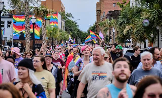 Group of people celebrating Pride in the street with rainbow flags in background