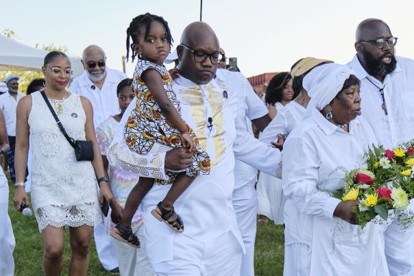 group of people in all white clothing carrying flowers