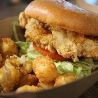 Fried chicken sandwich with lettuce and tomato and a side of tater tots