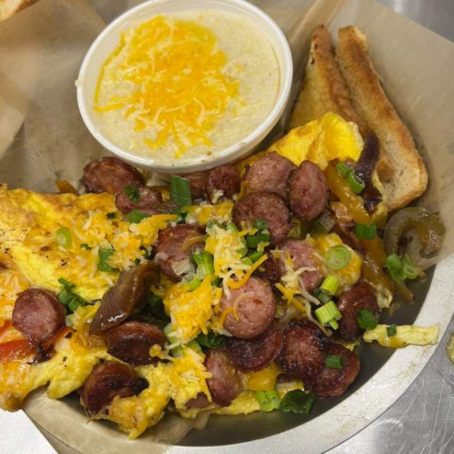 Omelet on a plate with sausage, cheese, green onions, toast and grits topped with cheese