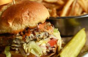 Close shot of burger, fries and a pickle spear