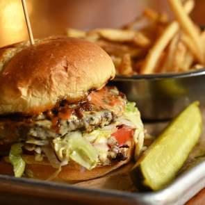 Close shot of burger, fries and a pickle spear