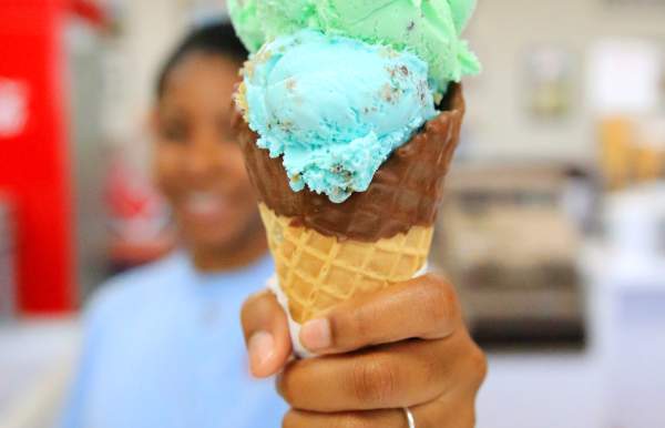 girl holding up a double scoop of ice cream in a waffle cone
