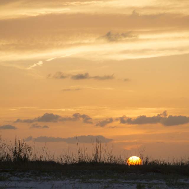 An orange sun sets behind the beach on Dauphin Island causing an orange sunset