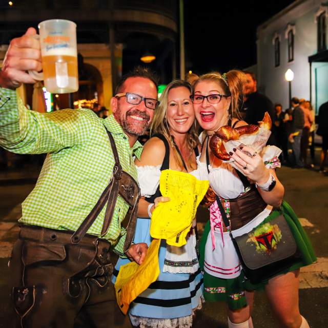 Two women and a man holding a beer bug and a pretzel