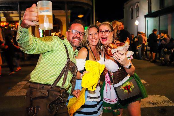 Two women and a man holding a beer bug and a pretzel
