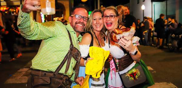 Two women and a man holding a beer bug and a pretzel