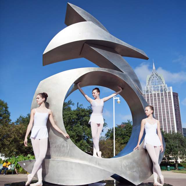 Three ballerinas posing on a steel sculpture