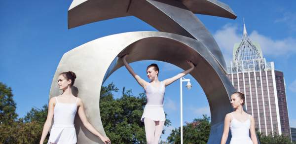 Three ballerinas posing on a steel sculpture