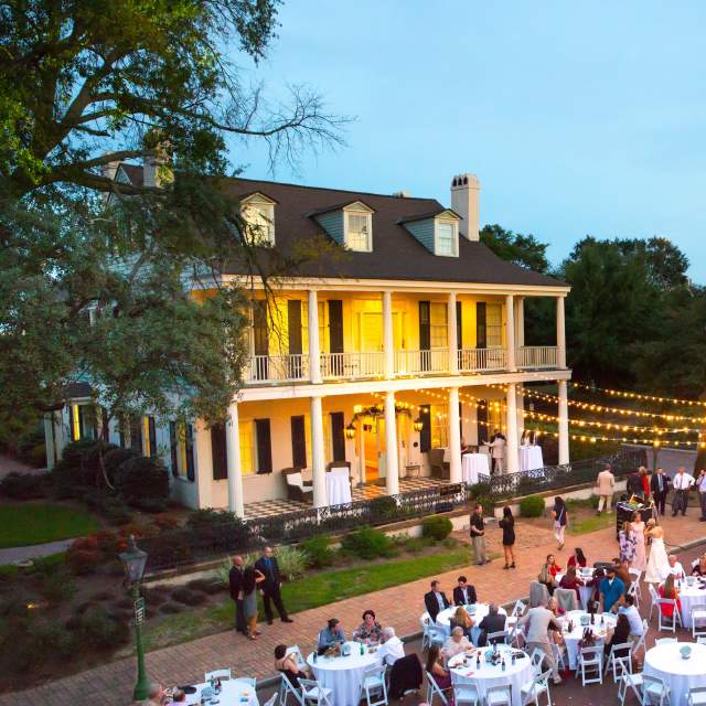 Large, Antebellum home with columns and string lights; round tables with people dining