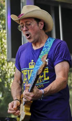 A man in a cowboy hat and purple shirt plays guitar