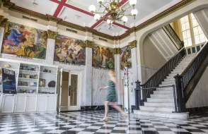 Woman in a blue dress crosses the lobby in front of a white marble staircase