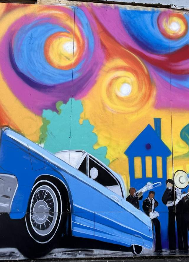 Mural of blue car in front of a rainbow sky and cityscape