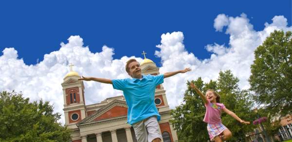 two small children running in front of a church holding their arms out like and airplane