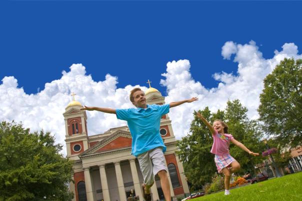 two small children running in front of a church holding their arms out like and airplane