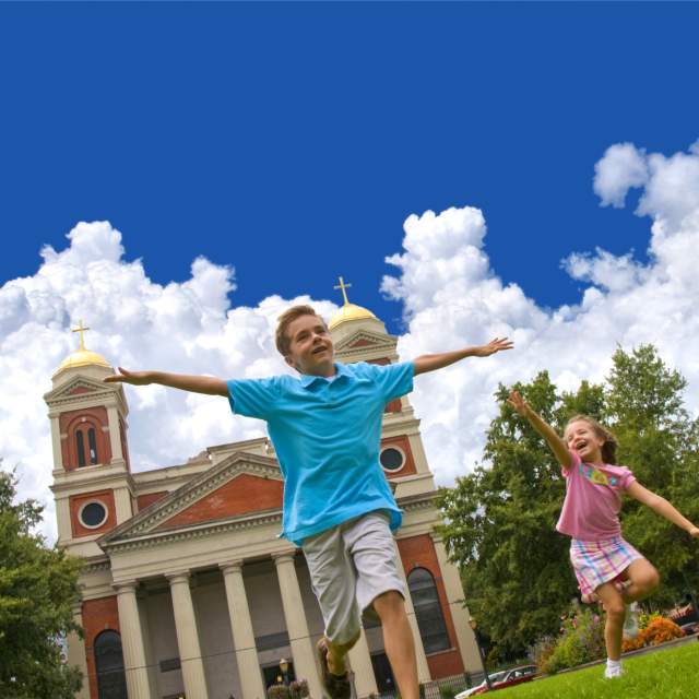 two small children running in front of a church holding their arms out like and airplane