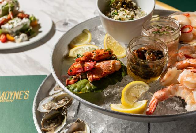 A tower of plates containing shrimp, oysters and seafood on ice with lemon and two glasses of white wine