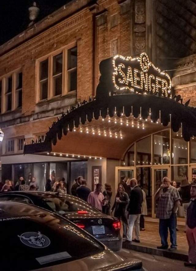 building with lighted entrance at night, people and cars outside