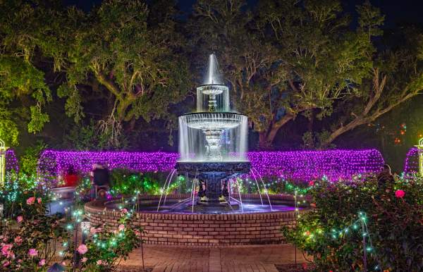An illuminated water fountain at nights surrounded by purple lights and Christmas decorations
