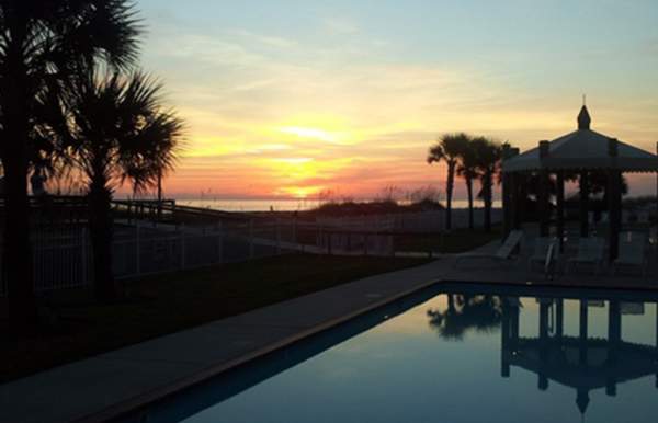 sunset over a pool and cabana with palm trees