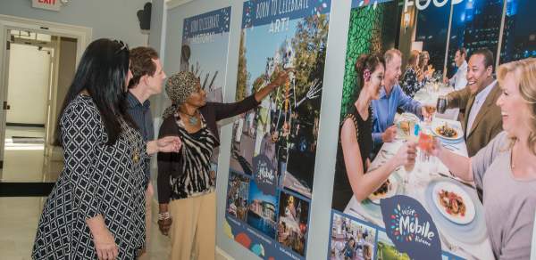 three people admiring wall hangings advertising Visit Mobile