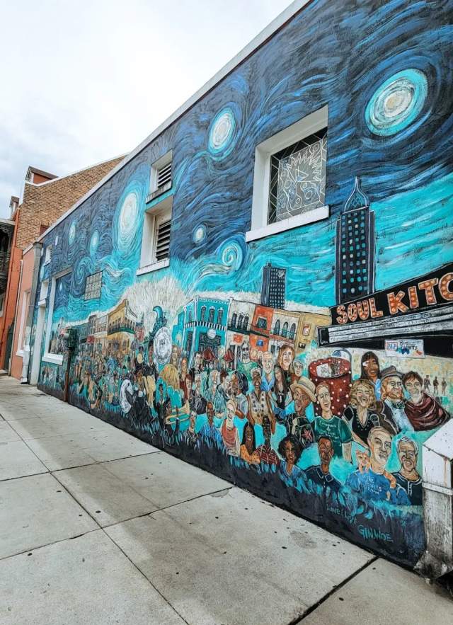 Swirly blue mural with the city behind a crowd of people