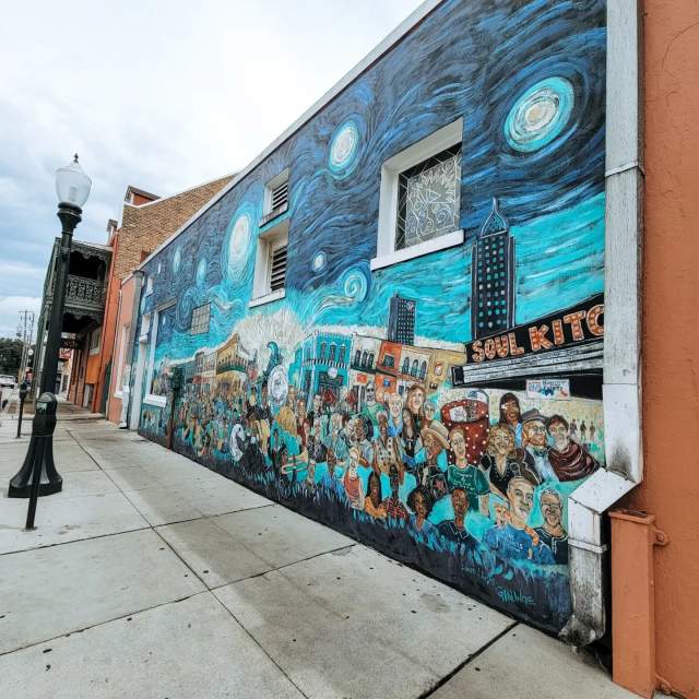 Swirly blue mural with the city behind a crowd of people