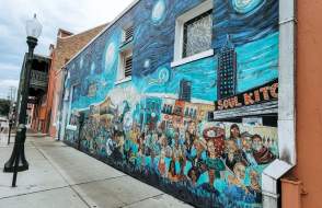 Swirly blue mural with the city behind a crowd of people