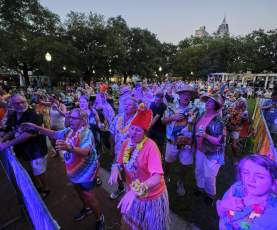 People dressed in tropical clothes dance at an outdoor music festival
