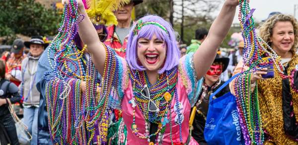 Woman in Mardi Gras costume holding beads and smiling