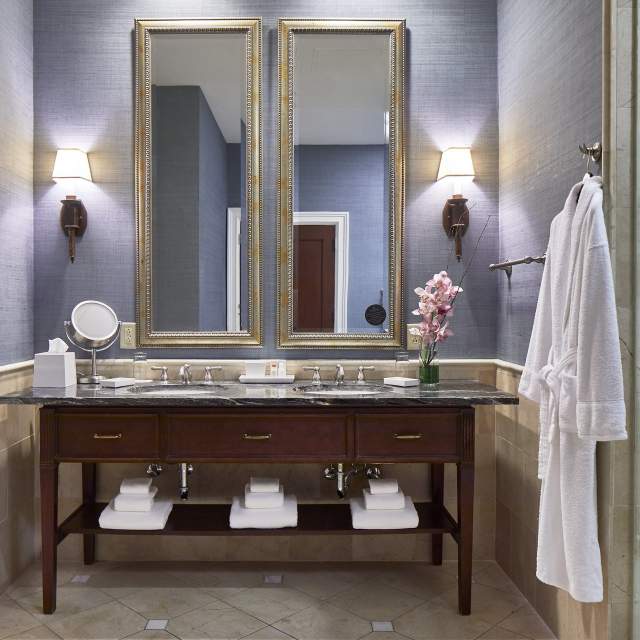 Hotel bathroom with double mirror over sink and robe hanging on the wall next to shower door