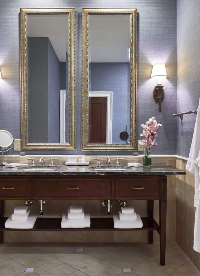 Hotel bathroom with double mirror over sink and robe hanging on the wall next to shower door