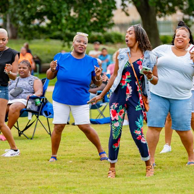 Four people dancing outdoors in front of a crowd of people