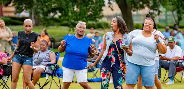 Four people dancing outdoors in front of a crowd of people