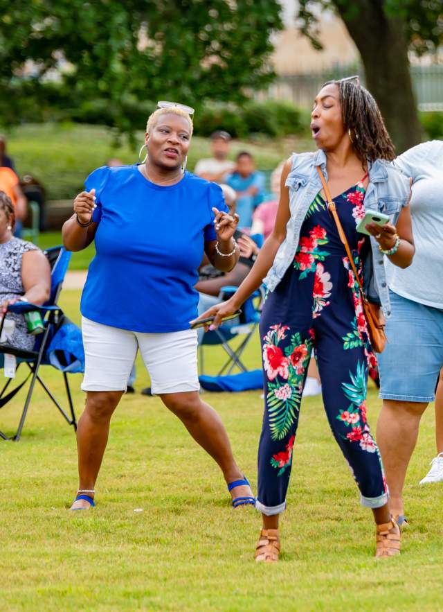Four people dancing outdoors in front of a crowd of people