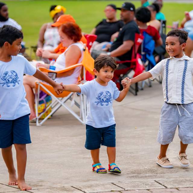 three children holding hands outside at an event