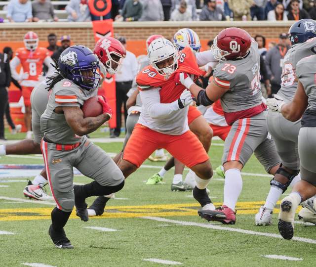 Football players in gray and orange jerseys, one player running with a football