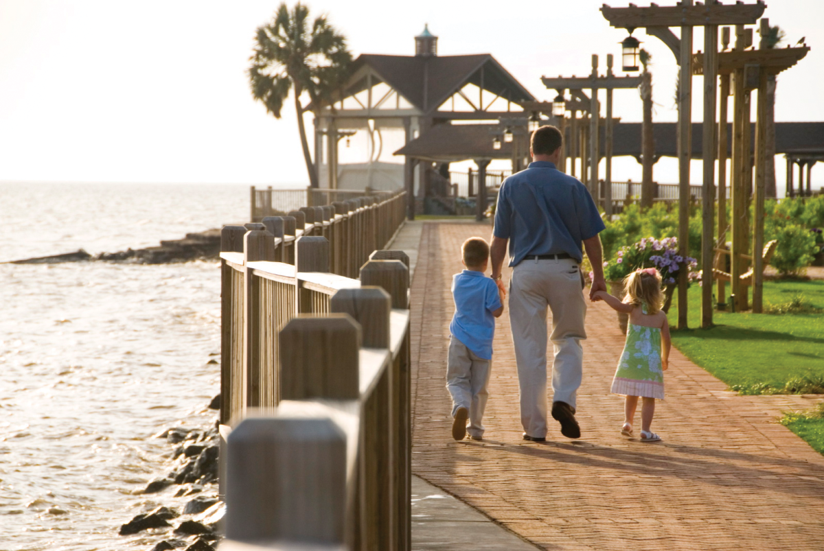 man and two small children walking along a sidewalk on the water's edge